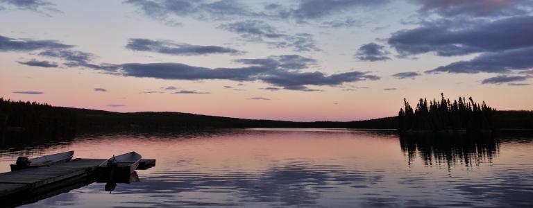 A calm lake at sunset with dock and motorboat in the shadows