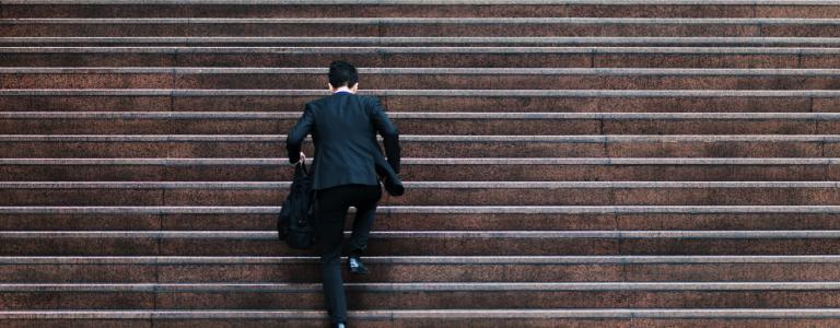 A man in a suit, seen from behind, runs up a large flight of steps