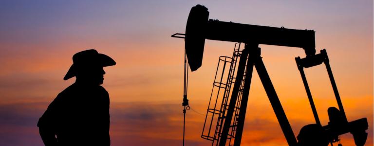 Silhouette of oil rig and cowboy in front of sunset sky