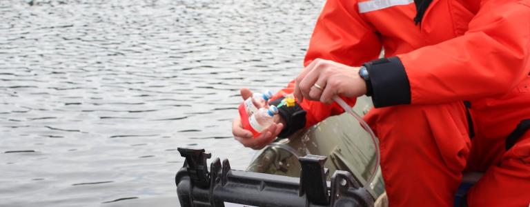 A researcher holds a collection sample over a lake