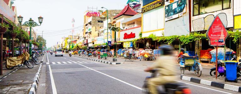 A person on a motorcycle drives down an urban street in Indonesia