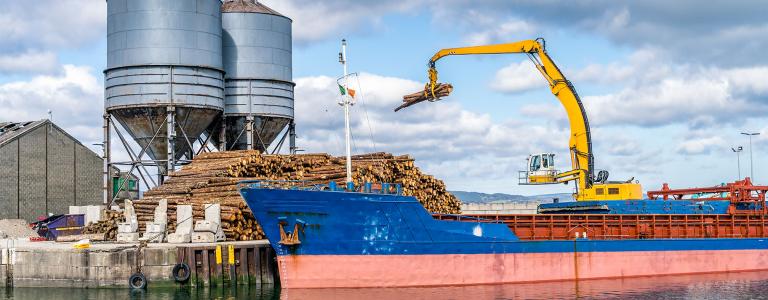 Crane with wood logs gripple loading timber on cargo ship for export in Wicklow commercial port. 