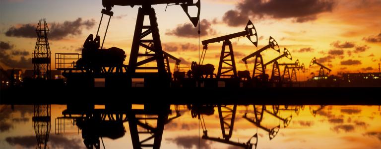 Oil wells are reflected on water at sunset.