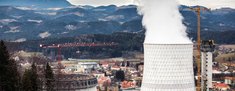 Smokestack emitting smoke against a city and mountain backdrop