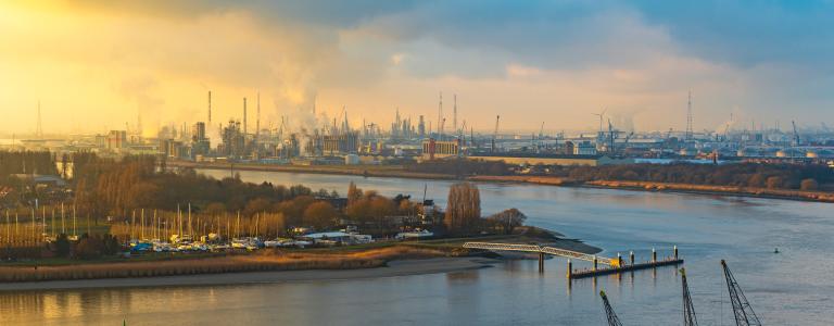 The second largest industrial harbor of Europe at sunset with cranes in the foreground, chemical and nuclear plants in the background and the Scheldt River, Antwerp, Belgium.