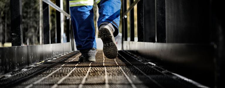 An oil rig worker walks away along a steel walkway.