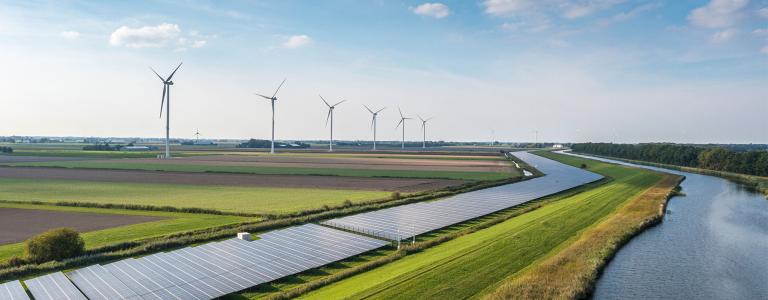 Wind turbines and solar panels operate next to a river.