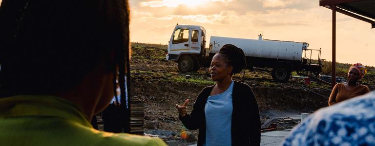 Women speaks to a gather group in front of a tank trunk. Photo credit: Jessica Meniere