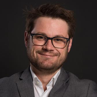 man smiling and wearing glasses and a gray suit