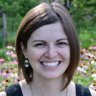 Woman with brown hait and white and gold earrings smiling into the camera